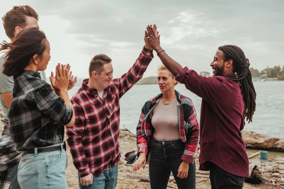 Disabled man with down syndrome high fiving support worker with group of friends